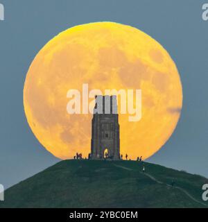 Glastonbury, Somerset, Großbritannien. Oktober 2024. Wetter in Großbritannien. Der volle Supermond der Hunters schwingt den St Michael’s Tower am Glastonbury Tor in Somerset, während er sich hinter dem Wahrzeichen erhebt, während sich eine Menschenmenge auf dem Hügel versammelt, um zu beobachten. Bildnachweis: Graham Hunt/Alamy Live News Stockfoto