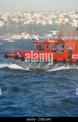Ein rotes Boot, das durch die Gewässer des Bosporus mit Istanbuls Stadtlandschaft im Hintergrund navigiert Stockfoto