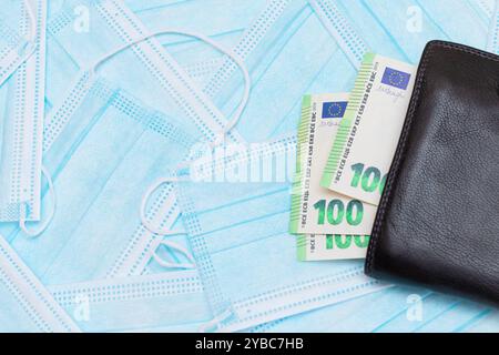 Schwarze Herren Brieftasche mit Euro Geld innen auf den blauen Einweg-medizinischen Gesichtsmasken. Handel mit medizinischen Masken. Unternehmen während einer Pandemie oder Epidemie Stockfoto