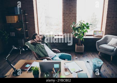 Ganzkörperfoto des jungen Mannes zerknitterte Papiere Müll kann sich entspannen Finish Arbeit Kleidung grünes Hemd modernes Bürozimmer Innenraum Arbeitsplatz Stockfoto