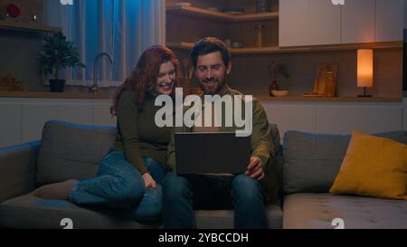 Glücklicher lächelnder kaukasischer Mann Ehemann Frau Frau heiratete Paare surfen Computer auf der Couch zu Hause entspannen romantischer Abend surfen Mediennetzwerk Stockfoto