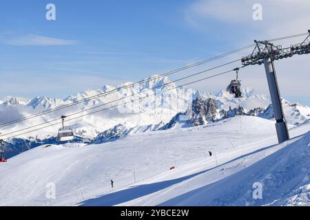 Atemberaubende Aussicht auf Sessellifte, die über schneebedeckte Berge in den drei Tälern hinaufsteigen. Skifahrer und Snowboarder im französischen Skigebiet Les Menuires. Stockfoto