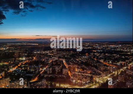 Ein atemberaubender Blick aus der Luft auf eine Stadtlandschaft in der Abenddämmerung mit beleuchteten Straßen und Gebäuden unter einem Dämmerungshimmel. Das Bild fängt das urbane Leben und das Leben ein Stockfoto