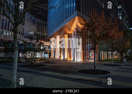 Ein modernes Bürogebäude, das bei Nacht beleuchtet wird, bietet moderne Architektur mit lebendiger Beleuchtung. Die Szene fängt das Wesen des urbanen Lebens ein Stockfoto