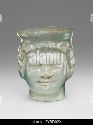 Janus-Head Cup, 1. Jahrhundert n. Chr. zusätzliche Info: Maltgeblasener Kolben aus blassgrünem Glas, in eine dreiteilige Form geblasen, bestehend aus zwei vertikalen Abschnitten, die mit einem scheibenförmigen Grundteil verbunden sind. Der Kolben ist zylindrisch mit Janiform-Verzierung. Die Gesichter sind pudgy und lächeln mit Efeukränzen um ihre Gesichter. Die Felge ist versetzt. Stockfoto