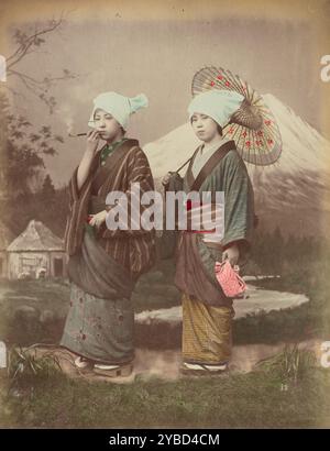 Japanische Reisende, 1870er-1890er Jahre Zwei junge Frauen, die Schals auf dem Kopf tragen. Einer raucht eine Pfeife und der andere trägt einen Sonnenschirm. Stockfoto