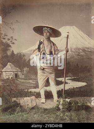 Pilger auf Fujiyama, 1870er-1890er Jahre Porträt eines Mannes mit breitem Hut und Wanderkleidung, der einen Wanderstock hält, vor einem Atelierhintergrund des Mt. Fuji. Stockfoto