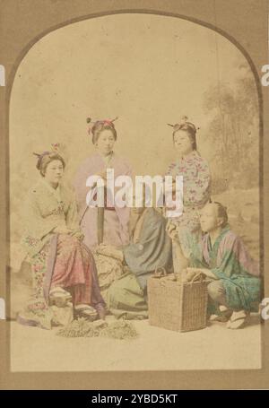 Gruppenporträt japanischer Frauen und Männer, 1868-1880. Gruppenporträt mit drei Frauen und zwei Männern, alle posierten vor einer bemalten Atelierkulisse. Die beiden Männer hocken sich vor der Gruppe, einer mit einem Korb voller Früchte vor sich, während er ein Stück der Frucht in einer Hand hält. Zwei der Frauen stehen hinter der Gruppe und die dritte Frau sitzt auf einem kleinen Felsbrocken auf der linken Seite des Bildes. Stockfoto