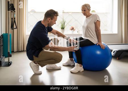 Männlicher Physiotherapeut, der ältere Frauen beim Stabilitätsballtraining im Heimgymnastikbereich führt. Zeigt personalisierte Betreuung, aktives Altern und Rehabilitation Stockfoto