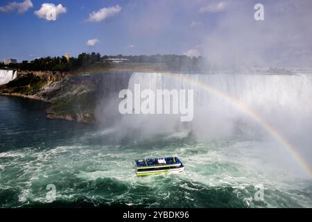 Ein Boot navigiert durch die Gewässer in der Nähe der Niagarafälle und zeigt einen wunderschönen Regenbogen über Ihnen. Stockfoto