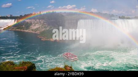 Ein Boot navigiert durch die Gewässer in der Nähe der Niagarafälle und zeigt einen wunderschönen Regenbogen über Ihnen. Stockfoto