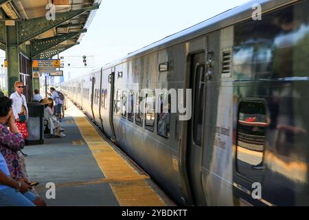 Woodside, New York, USA - 20. August 2024: Long Island Railroad Train verlässt den Bahnhof Woodside Queens, während Leute auf dem Bahnsteig warten. Stockfoto