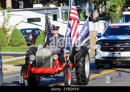 Hauppauge, New York, USA - 5. Oktober 2024: Ein örtlicher Freiwilliger Feuerwehrmann reitet stolz mit Fahnen in einem Traktor während der Heimfeierparade. Stockfoto