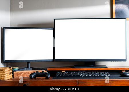 Zwei Computermonitore mit leeren Bildschirmen auf einem Holzpult, mit Tastatur und Gamecontroller. Stockfoto