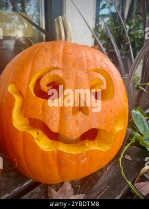 Eine skurrile Jack-o'-Laterne mit spiralförmigen Augen und einem lächelnden Gesicht, die in einen leuchtend orangen Kürbis geschnitzt ist, verleiht der Halloween-Dekoration einen verspielten Touch Stockfoto