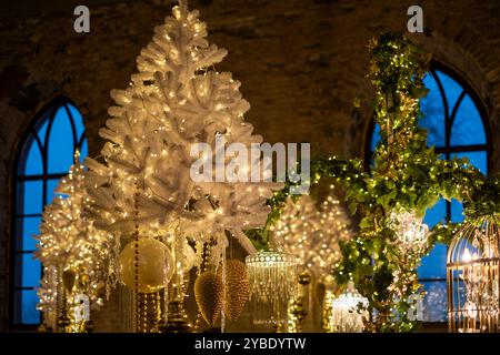 Die gemütliche Inneneinrichtung zeigt einen weißen Weihnachtsbaum mit funkelnden Lichtern, umgeben von komplizierten Weihnachtsdekorationen und sanfter Beleuchtung Stockfoto