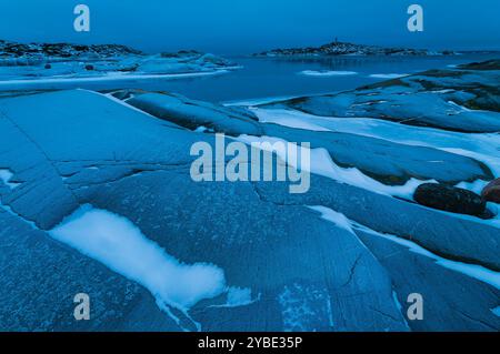 Die zerklüftete Küste in der Nähe von Göteborg, Schweden, bietet glatte, eisige Felsen und sanfte Wellen unter einer ruhigen blauen Winterdämmerung, die ein Gefühl der Ruhe wecken Stockfoto