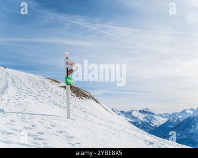 Ein Wegweiser an einem schneebedeckten Bergweg in den französischen Alpen, der die Wegbeschreibung nach Briancoon und Pelvoux anzeigt. Die Szene ist hell und klar, mit Fußabdrücken Stockfoto