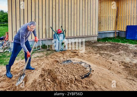 Nachdem der Arbeiter eine Böschung um die Lukenabdeckung angelegt hat, verdichtete er Sand mit einer Schaufel. Stockfoto