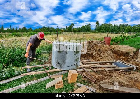 Der Arbeiter bewegt den Betonring mit einem Rollendeck aus Stahlrohren und -Brettern. Stockfoto