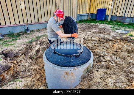 Der Baumeister trägt eine Mannlochabdeckung, die gut aus Betonringen besteht. Stockfoto