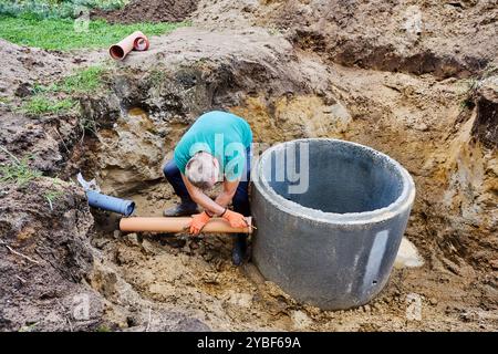 Der Arbeiter verbindet das Einlasskanalrohr mit dem Klärsystem, nachdem er zuerst die Stelle für das Loch im Betonring markiert hat. Stockfoto