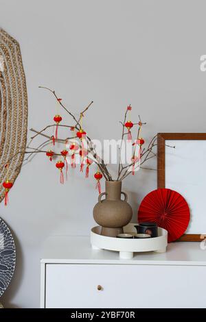 Vase mit Baumzweigen, chinesischen Laternen und Tee auf Kommode im Wohnzimmer. Chinesisches Neujahrsfest Stockfoto