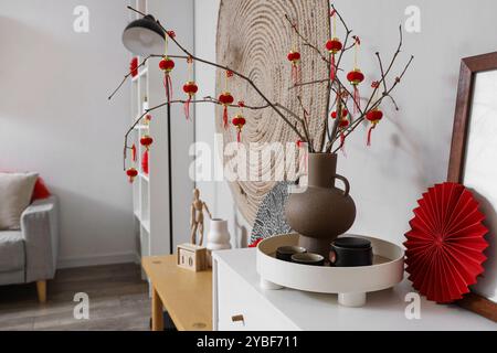 Vase mit Baumzweigen, chinesischen Laternen und Tee auf Kommode im Wohnzimmer. Chinesisches Neujahrsfest Stockfoto