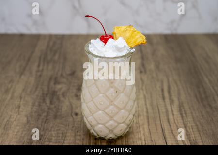 Pina Colada mit süßer Verkostung, serviert in Ananasglas und garniert mit Schlagsahne, Kirsche und Orange. Stockfoto