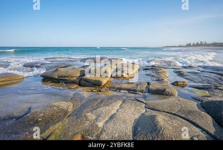 Blick nach Süden entlang des Buddina Beach mit Meereswellen, die über die felsige Uferplattform brechen, während die Brandung in Point Cartwright, Sunshine Coast, einrollt Stockfoto