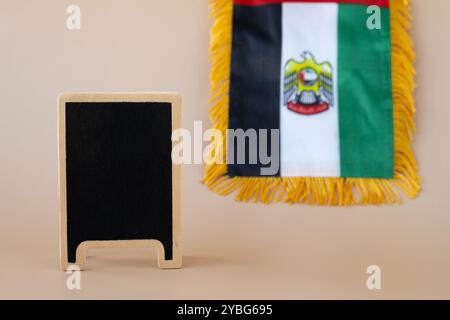 Leere Tafel Vorlage nationales Symbol der VAE. Kleine Flagge der Vereinigten Arabischen Emirate mit Wanderfalke auf neutralem beigem Hintergrund. Kopieren Sie den Platz für Ihren Text. Das Konzept der Unabhängigkeit des Nationaltages Stockfoto