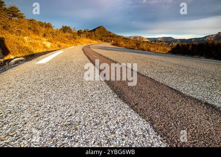 Straße bei Sonnenaufgang mit einer dunkleren Linie von neuem Asphalt, die sich vom benutzten Asphalt abhebt, im Departement Var, Frankreich, Europa. Stockfoto