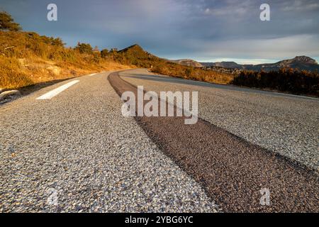 Straße bei Sonnenaufgang mit einer dunkleren Linie von neuem Asphalt, die sich vom benutzten Asphalt abhebt, im Departement Var, Frankreich, Europa. Stockfoto
