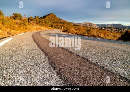 Straße bei Sonnenaufgang mit einer dunkleren Linie von neuem Asphalt, die sich vom benutzten Asphalt abhebt, im Departement Var, Frankreich, Europa. Stockfoto