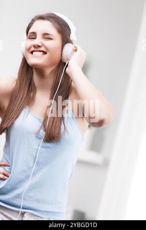 Die junge Frau tanzt zu Hause und hört Musik mit Kopfhörern in einem modernen, hellen Raum. Sie verströmt eine sorglose, fröhliche Atmosphäre in ihrem Minimalist Stockfoto