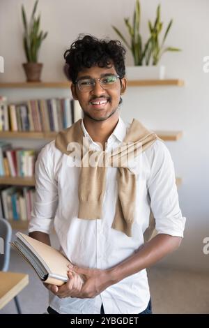Fröhlicher indischer Student in Brille, der für vertikales Porträt steht Stockfoto
