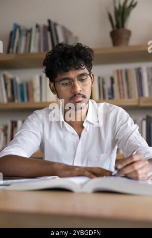 Ernsthafter junger indischer Student, der an wissenschaftlichen artikeln arbeitet Stockfoto