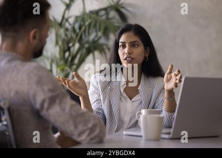 Ernsthafte junge indische Geschäftsberaterin, die mit männlichen Kunden spricht Stockfoto