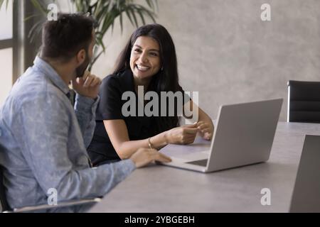 Glückliche Geschäftsfrau aus dem Nahen Osten, die mit der Kollegin am Laptop spricht Stockfoto