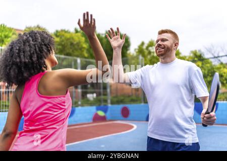Multirassische Frauen- und Männerteams sind High-Fiving, während sie beim Pickleball feiern Stockfoto