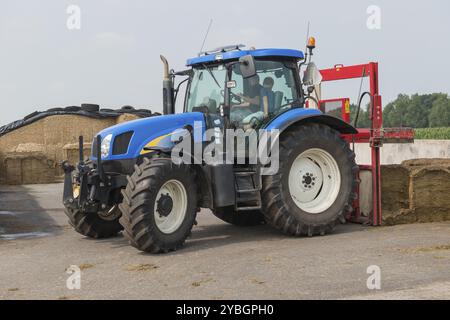 Blaue Traktor mit einem roten Ballen Hobel zum Abschneiden Silageballen Stockfoto