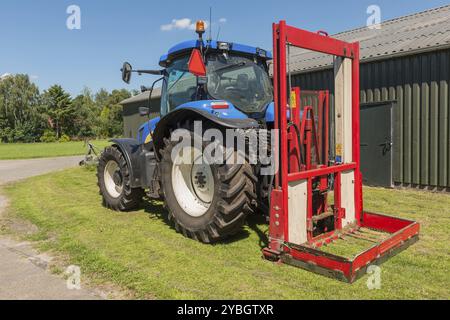 Blaue Traktor mit einem roten Ballen Hobel zum Abschneiden Silageballen Stockfoto