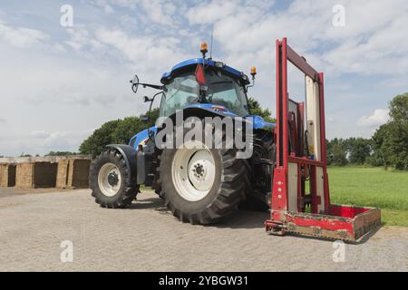 Blaue Traktor mit einem roten Ballen Hobel zum Abschneiden Silageballen Stockfoto