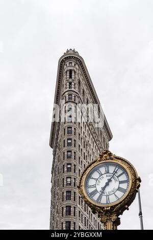 New York City, USA, 20. Juni 2018: Flatiron Building in Manhattan. Niedriger Winkel bei bewölktem Tag mit Uhr im Vordergrund. Es ist eine der Welten Stockfoto