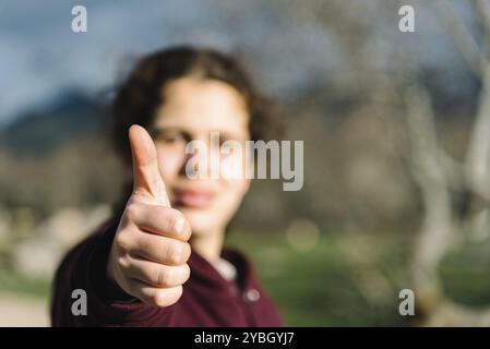 Schöne junge erwachsene Frau, Daumen nach oben Geste. Fokus auf der Hand. Unscharfer Natur Hintergrund Stockfoto