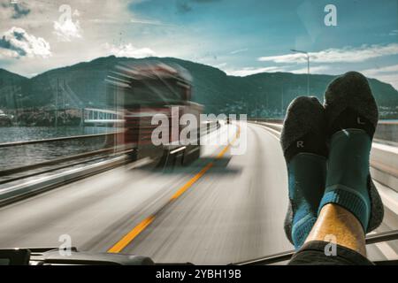 Roter Lastwagen auf einer Brücke im Gegenverkehr, die Füße des Beifahrers auf der Windschutzscheibe, Europastraße E39, Vagseidet, Norwegen, öffentliches Gelände, Europa Stockfoto