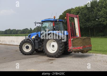 Blaue Traktor mit einem roten Ballen Hobel zum Abschneiden Silageballen Stockfoto