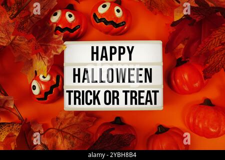 Happy Halloween und Trick or Treat Text in Leuchtkasten mit Ahornblatt und Kürbisse Dekoration auf orangem Hintergrund Stockfoto