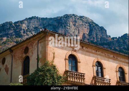 Ein wunderschönes historisches Steingebäude mit Bogenfenstern und einer malerischen Bergkulisse unter klarem Himmel, die ein Gefühl von zeitloser Eleganz und nat weckt Stockfoto