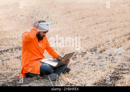 Indischer ländlicher Landwirt, der auf dem Feld der Feldfrüchte an einem Laptop arbeitet Stockfoto